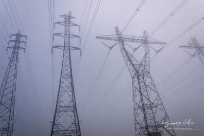 JCCI-100608 - Towering electrical power pylons disappearing into thick fog landscape