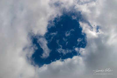 JCCI-100627 - A hole through thick fluffy white clouds showing the deep blue sky behind