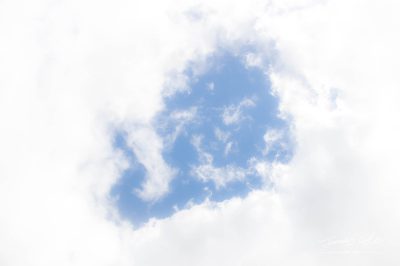 JCCI-100628 - A hole through glowingly bright fluffy white clouds showing the pale blue sky behind