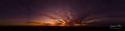 JCCI-100635 - Dark wispy clouds in a deep purple sky at the end of a glowing orange sunset aerial panoramic