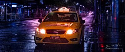 A Melbourne City yellow taxi cab on a rainy night with wet streets and light glows