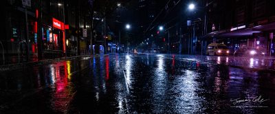 An empty rainy city street at night with lights reflecting in puddles in Melbourne
