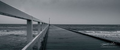 A lonely desolate pier juts out to a moody sea on a sombre rainy day in Black and White